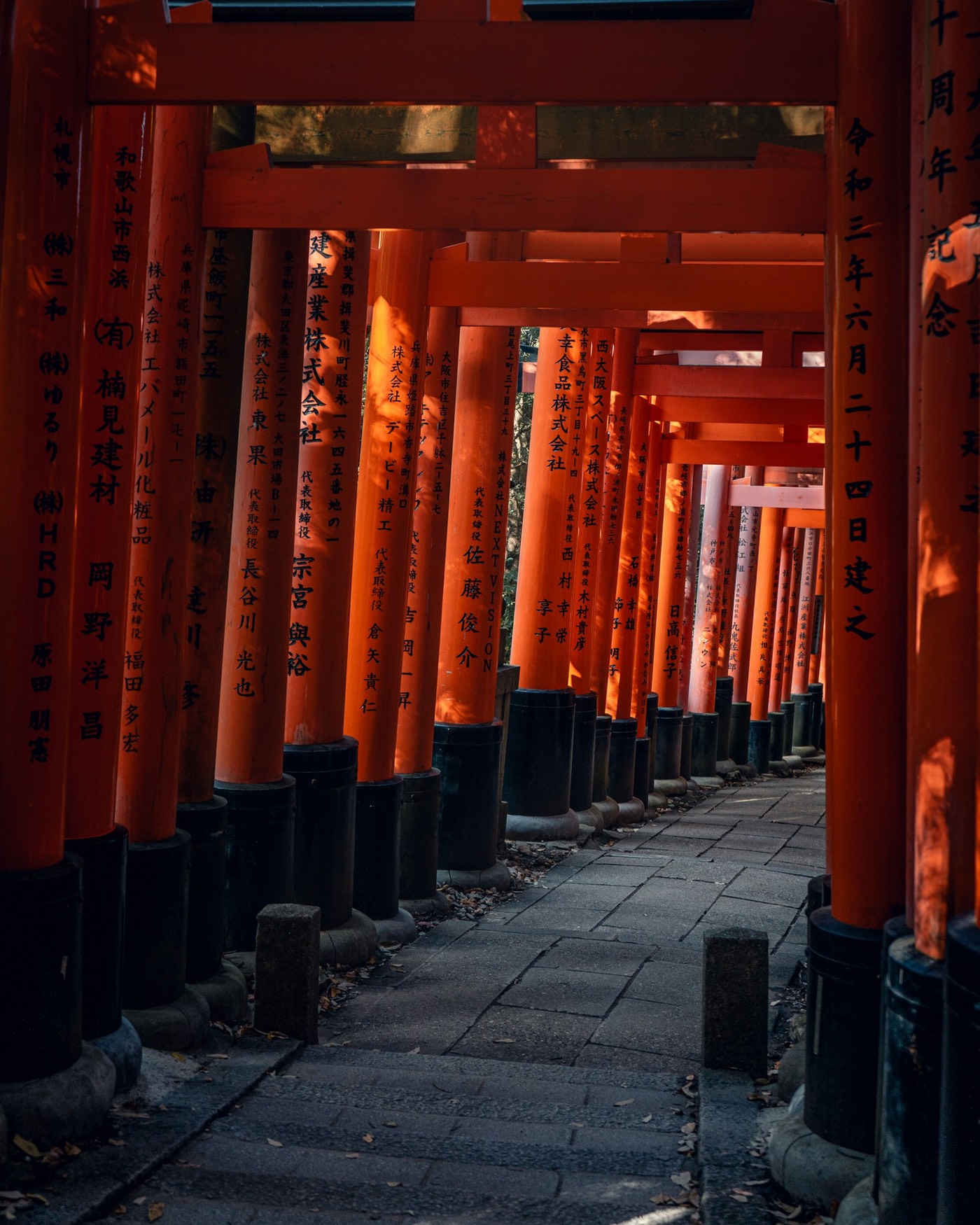 A stone path through rows of orange torii gates in Kyoto